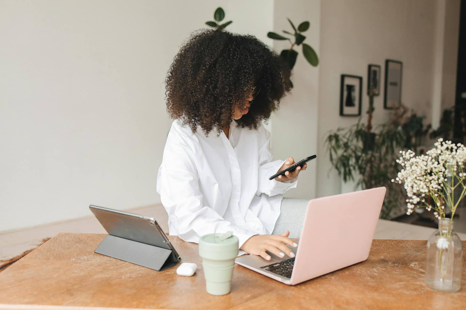 Young woman multitasking at home using laptop, tablet, and smartphone in a cozy indoor setting.